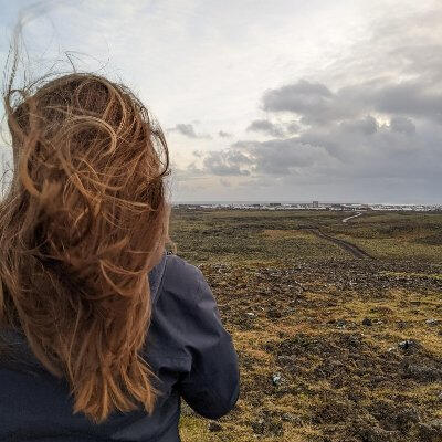 Picture of woman with long hair blowing in the wind, looking out across rocky landscape at Grindavik, Iceland